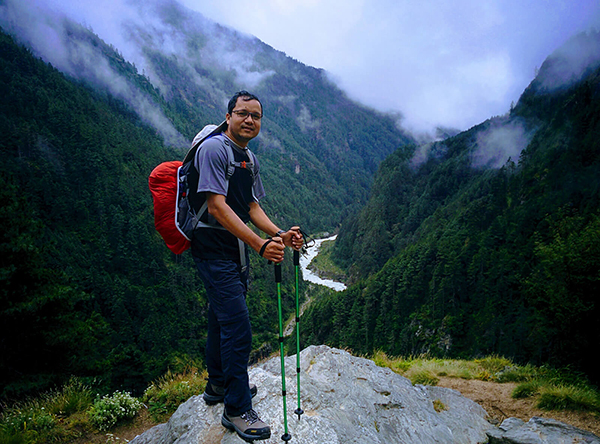 Billal hiking with trekking poles above a river in a misty mountain valley